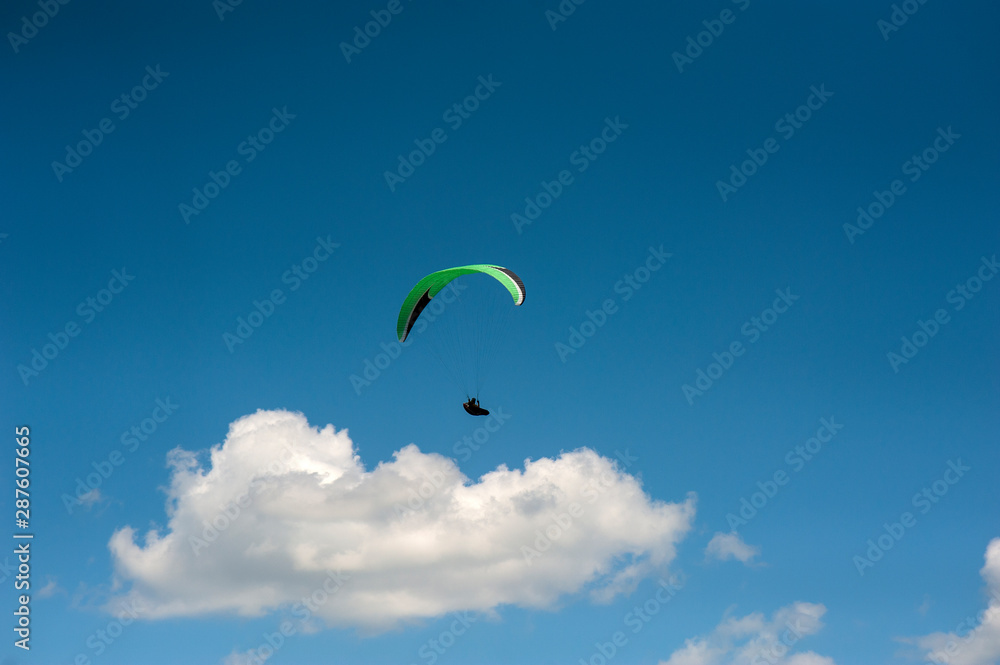 Alone paraglider flying in the blue sky against the background of clouds. Paragliding in the sky on a sunny day. Alone paraglider flying in the blue sky against the background of clouds. Paragliding in the sky on a sunny day.
