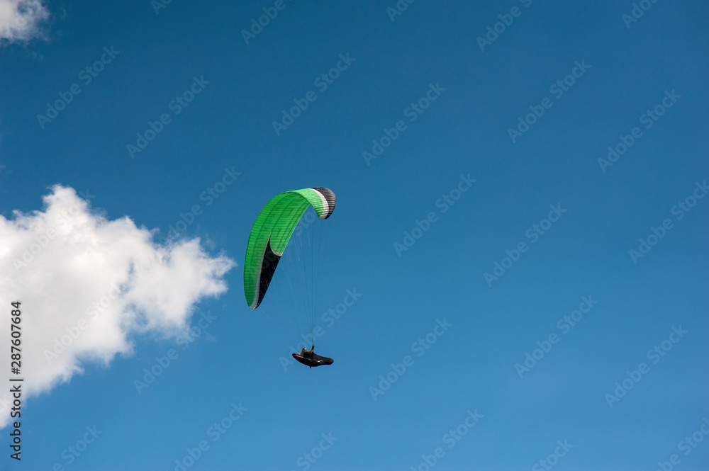 Alone paraglider flying in the blue sky against the background of clouds. Paragliding in the sky on a sunny day. Alone paraglider flying in the blue sky against the background of clouds. Paragliding in the sky on a sunny day.