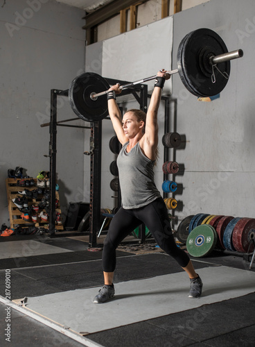 Fotografía Strong female weight lifter with heavy barbell over her head.