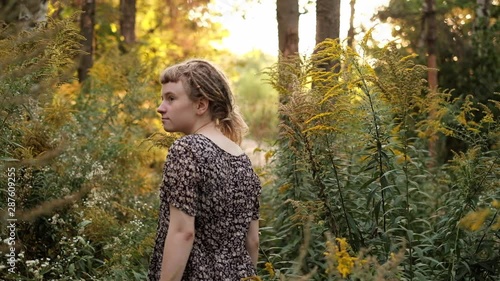 Girl walks through beautiful wild flowers in the forest with the morning sun picking through in the background. Trendy hipster girl with dreadlocks enjoying nature photo