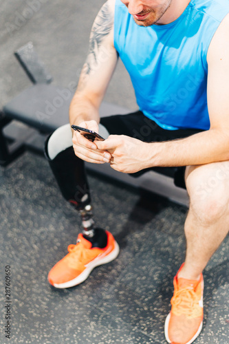 Disabled athlete resting with leg prosthesis. He is texting on his phone