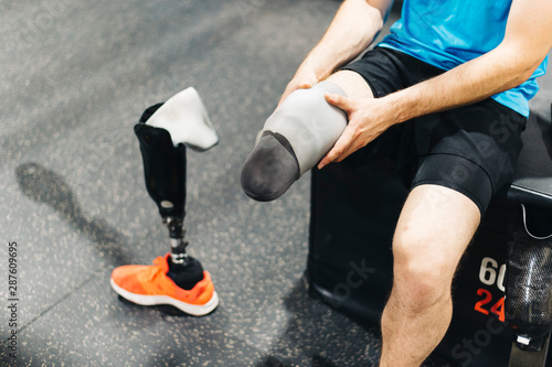 Disabled athlete assembling his leg prosthesis in the gym. Paralympic Sport Concept.