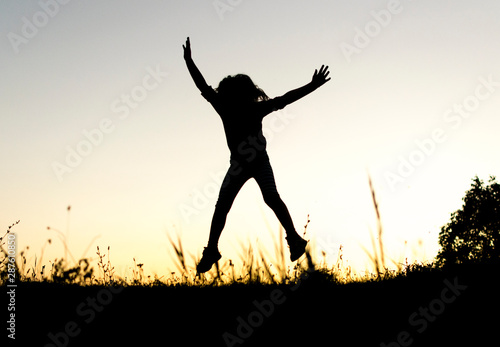 Silhouete of small girl running and jumping on top of the hill