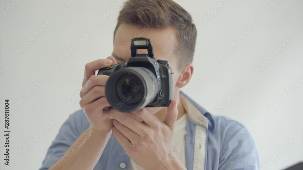 Portrait of photographer taking photos while sitting on the chair and looking at camera. Photographer taking photos on white background in the studio. Fashion magazine studio photoshoot. Portrait of photographer taking photos while sitting on the chair and looking at camera. Photographer taking photos on white background in the studio. Fashion magazine studio photoshoot.