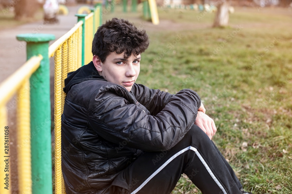 A young teenager sits on the grass and smiles, he is glad that the fall has started, it is no longer hot and he can play outdoor sports A young teenager sits on the grass and smiles, he is glad that the fall has started, it is no longer hot and he can play outdoor sports