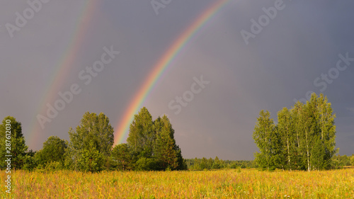 Large panorama of the rainbow landscape over the field on a summer day
