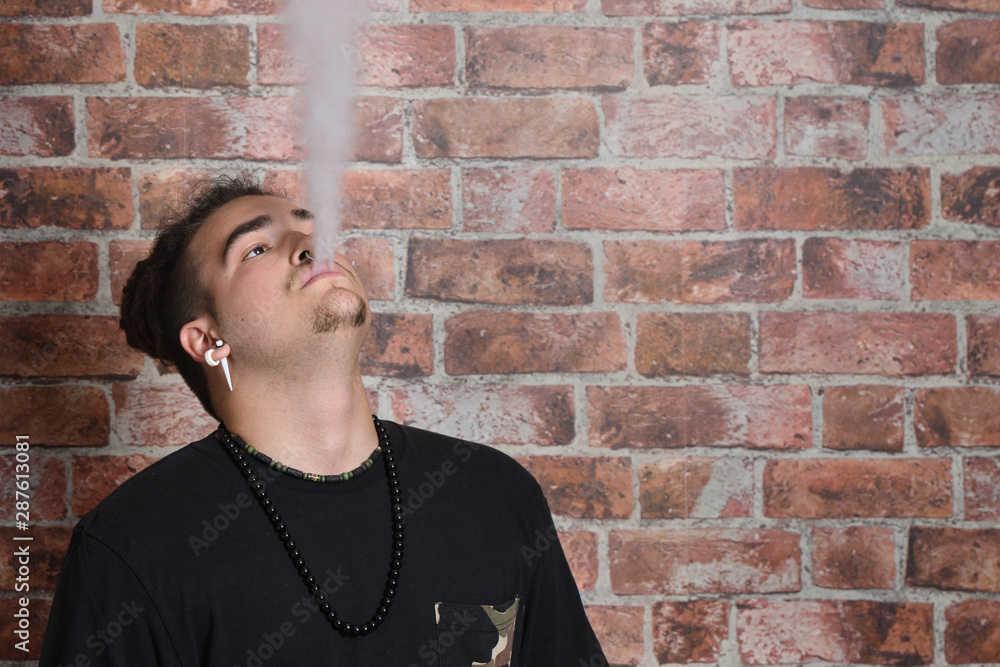 Vaper Smoke outdoor electronic cigarette near the brick wall. Young man smoking big cloud of steam Vaper Smoke outdoor electronic cigarette near the brick wall. Young man smoking big cloud of steam