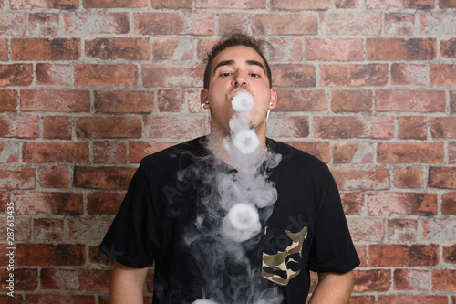 Vaper Smoke outdoor electronic cigarette near the brick wall. Young man smoking big cloud of steam
