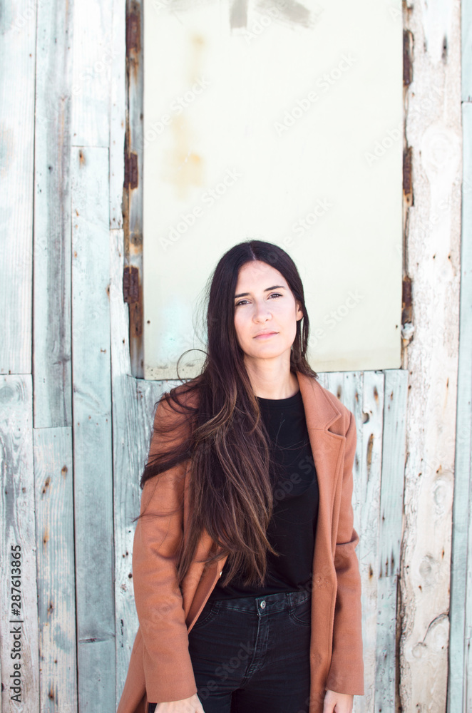 Fototapeta premium long-haired young woman wears trench coat and looks at camera
