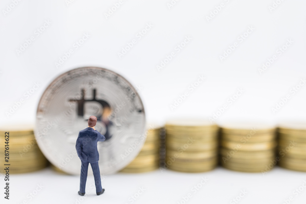 Business, e-commerce, crypto currency, finance and technology concept. Close up of businessman miniature figure standing and looking to bitcoin coin and row of stack of gold coin on white background.