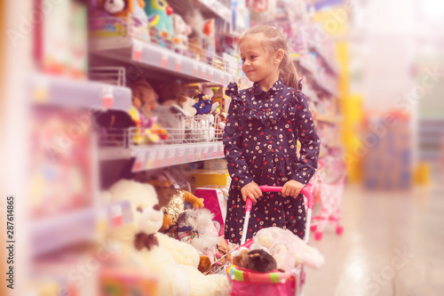 Little girl selecting toys on shelves in supermarket.