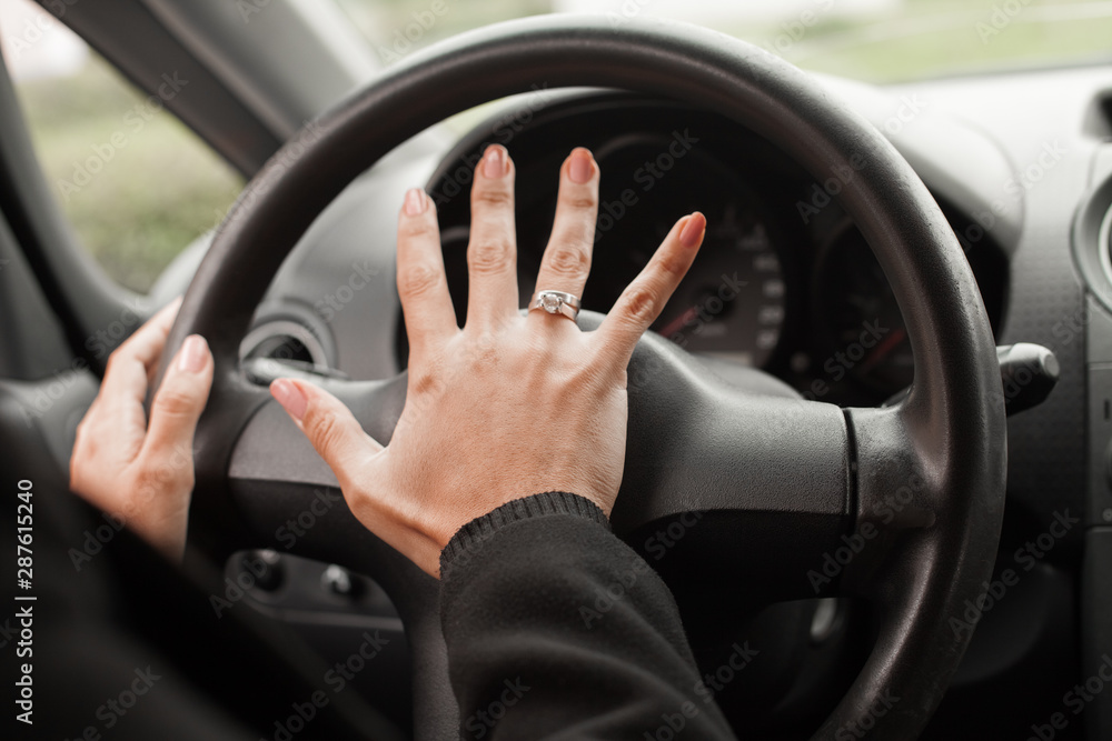 Closeup inside vehicle of hand pushing on steering wheel honking horn, female driver concept