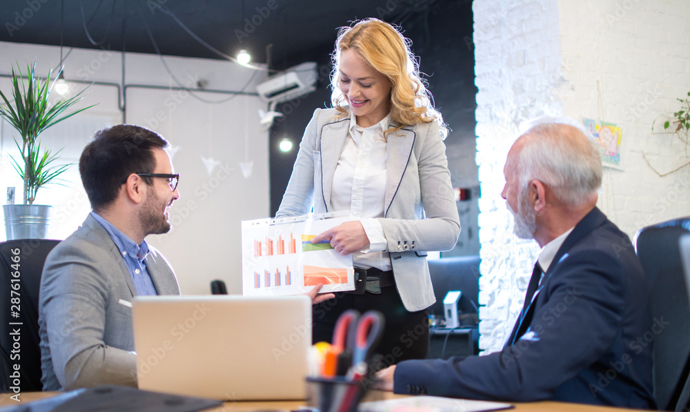 Mature businesswoman in businesswear showing graphs to her business partners on a meeting in office Mature businesswoman in businesswear showing graphs to her business partners on a meeting in office