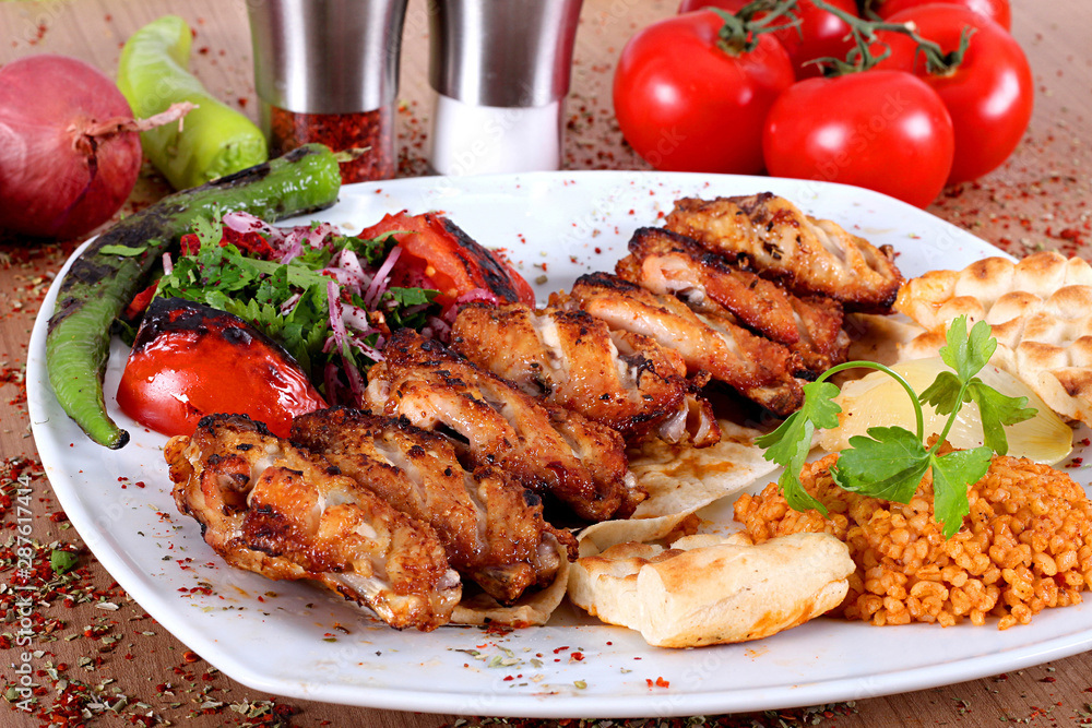 Roasted chicken wings served on a white plate with peppers onions tomatoes and salads