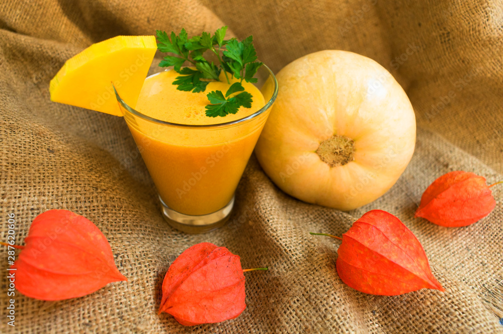  Glasses of fresh pumpkin juice and pumpkin on a table decorated with physalis flowers. The concept of healthy seasonal smoothies.
