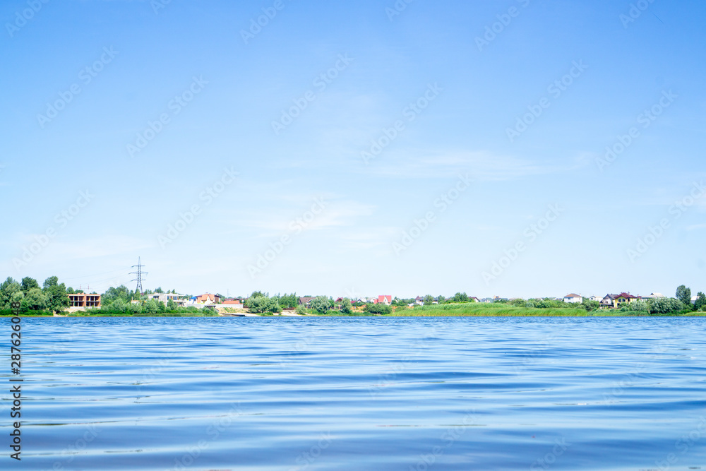 Private houses with red roofs on the horizon. River and blue sky. In the light. light tone. Horizontal orientation