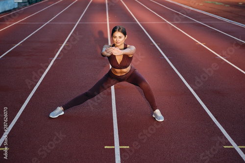 Beautiful sporty girl in sportswear doing stretching exercises on stadium. Fitness woman doing warm up workout outdoor