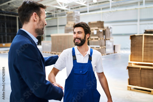 Businessman and worker shaking hands in a factory