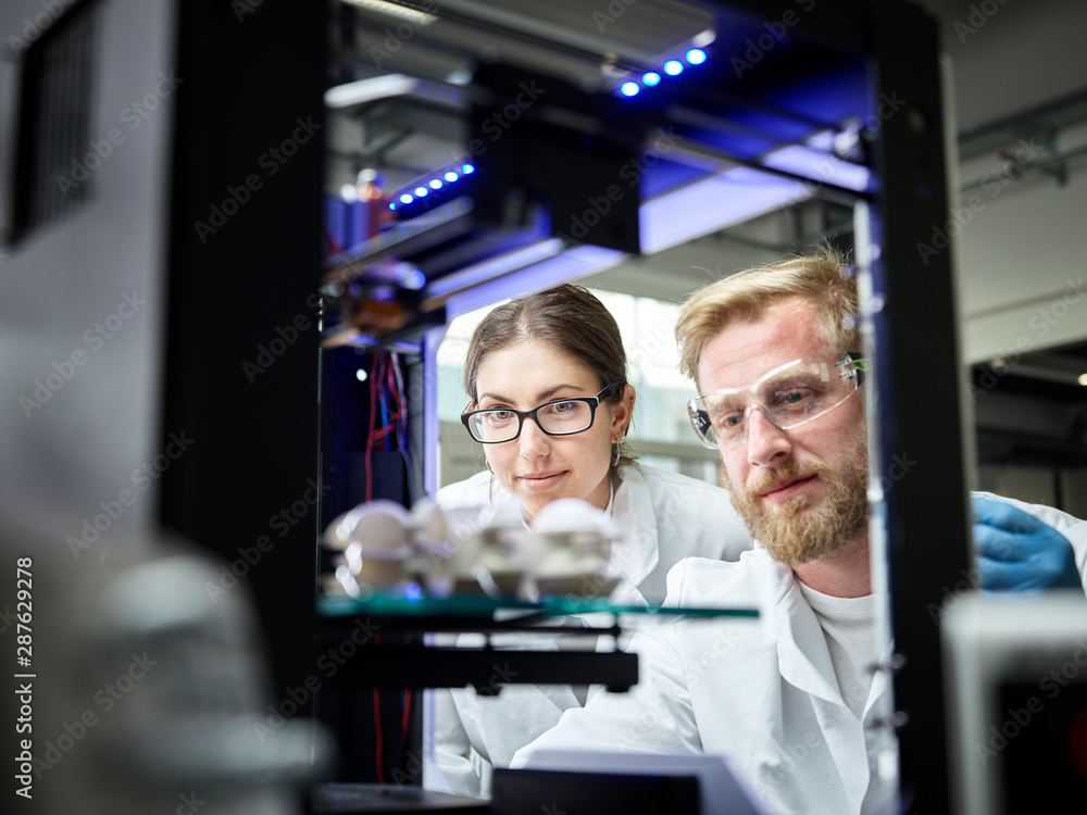 Two technicians looking at turbine wheel being printed in d printer Two technicians looking at turbine wheel being printed in d printer