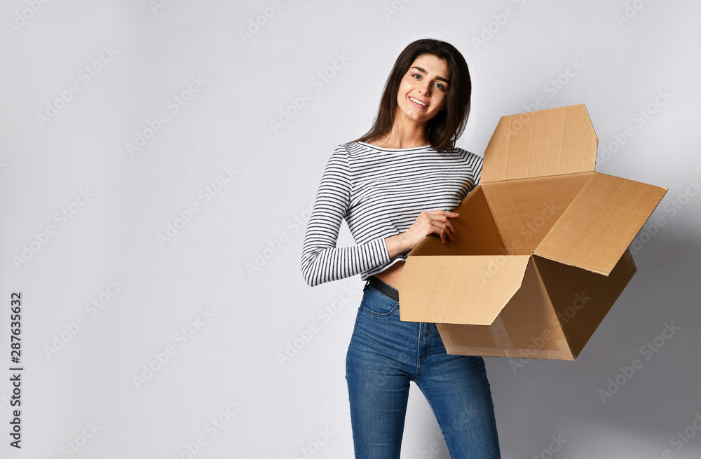beautiful brunette woman standing on a light background with a moving cardboard box beautiful brunette woman standing on a light background with a moving cardboard box