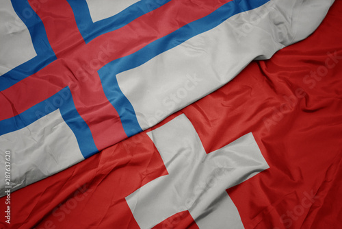 waving colorful flag of switzerland and national flag of faroe islands.