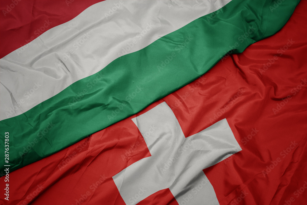 waving colorful flag of switzerland and national flag of hungary.