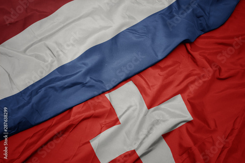 waving colorful flag of switzerland and national flag of netherlands.