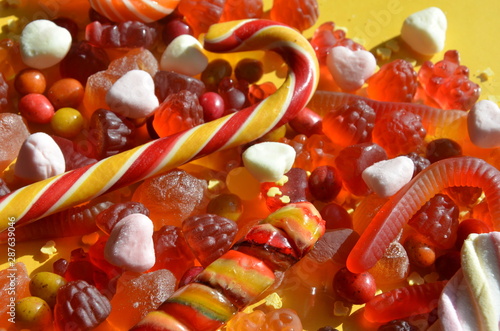 candies with jelly and sugar. colorful array of different childs sweets and treats on yellow background. red marmalade in the shape of a heart with a variety of caramels and candies, marshmallows.