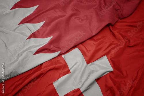 waving colorful flag of switzerland and national flag of bahrain.