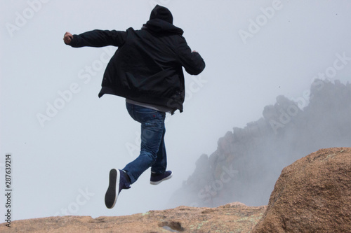 boy jumping off foggy moountain