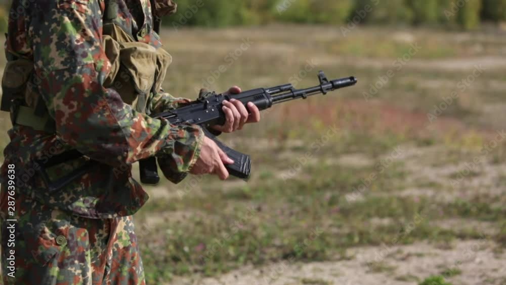 A man in camouflage prepares weapon for shooting. Opens butt, charges a magazine with bullets into Kalashnikov rifle and distort the shutter. AK47 loading Close-up. Soldier hand charging machine gun A man in camouflage prepares weapon for shooting. Opens butt, charges a magazine with bullets into Kalashnikov rifle and distort the shutter. AK47 loading Close-up. Soldier hand charging machine gun