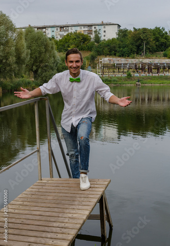 young man with a green bow-tie on a bridge on a lake background