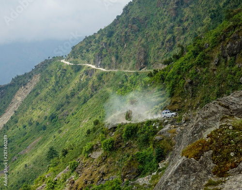 Tourists on road trip to Tibet drive a jeep down a dirt road in the Himalayas. © helivideo