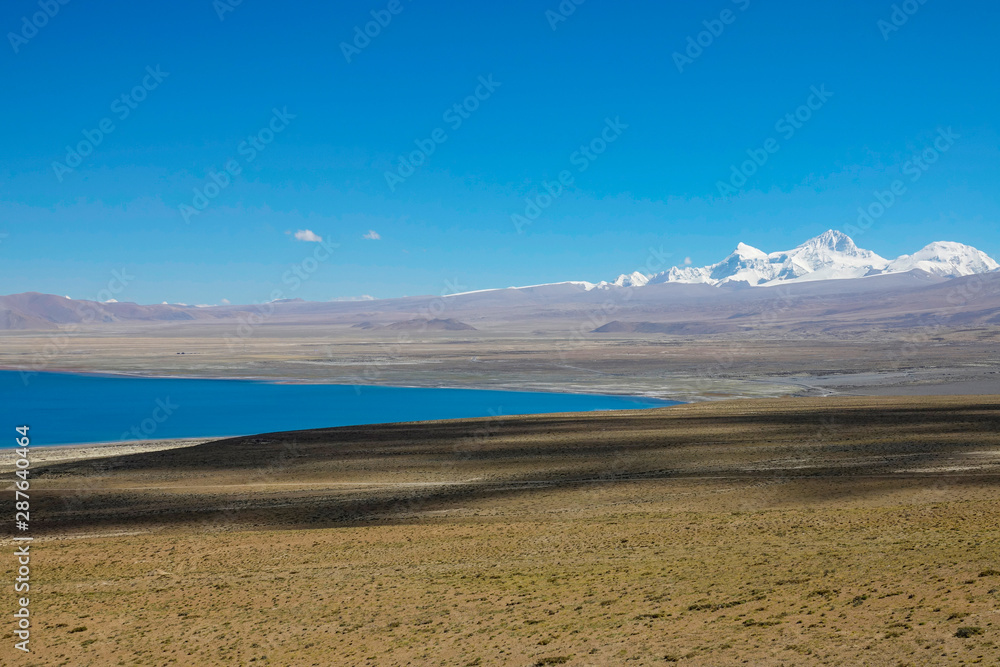 Picturesque shot of an emerald lake in barren Tibetan plains and snowy mountains Picturesque shot of an emerald lake in barren Tibetan plains and snowy mountains