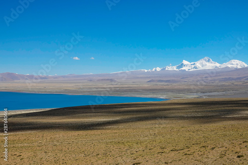 Picturesque shot of an emerald lake in barren Tibetan plains and snowy mountains