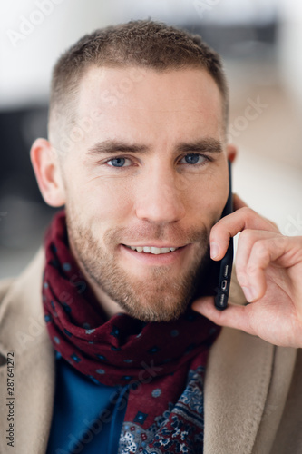 Young serious man wearing scarf and coat talking on mobile phone close-up.
