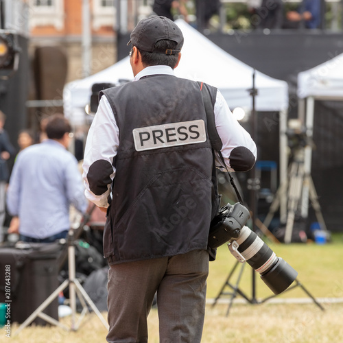 Rear View of Man Carrying Camera Wearing a Jacket With the Word 