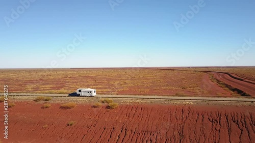 Aerial panoramic view of cars traveling on highway in Australia, with vast red arid outback landscape, sunny blue sky and horizon as background.