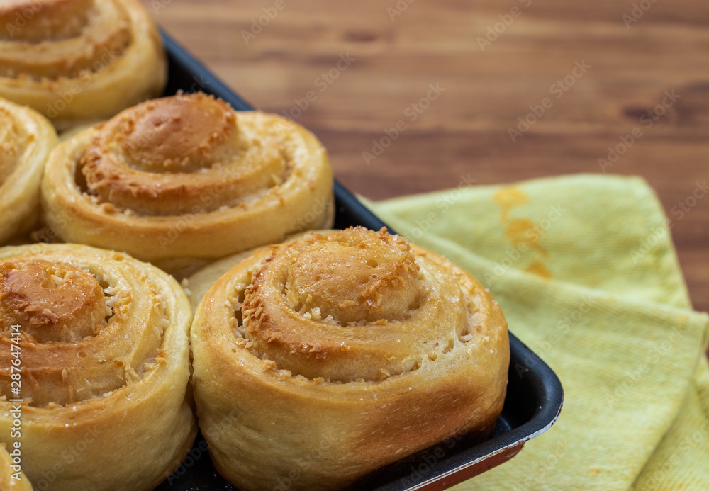 Twisted buns made of yeast dough with cinnamon, cane sugar and coconut flakes on a black baking sheet, bokeh, close-up, side view from above