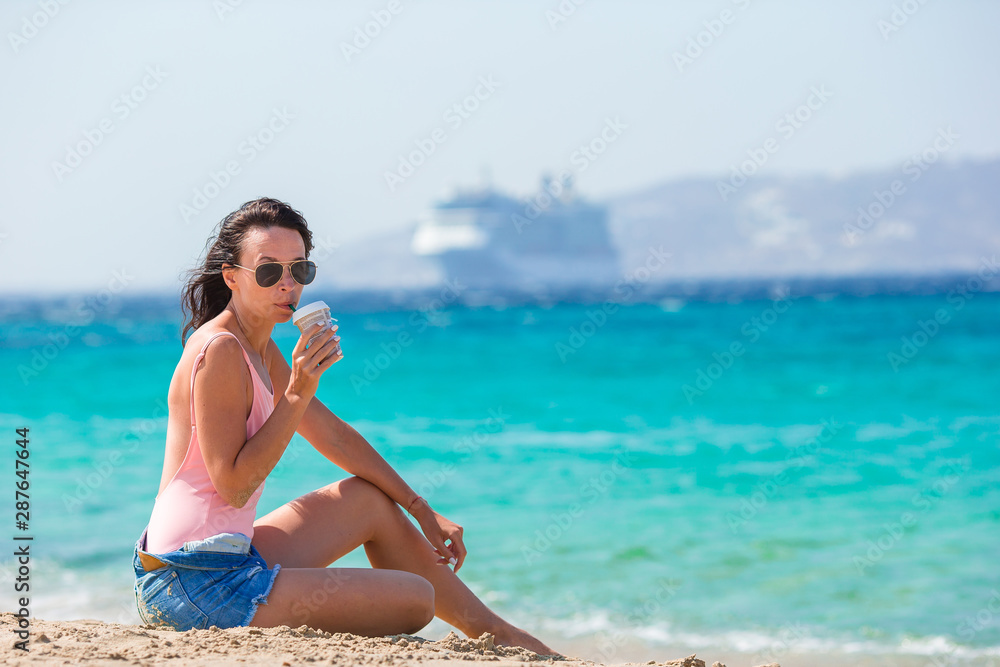 Young beautiful woman with coffee on the beach during tropical summer vacation