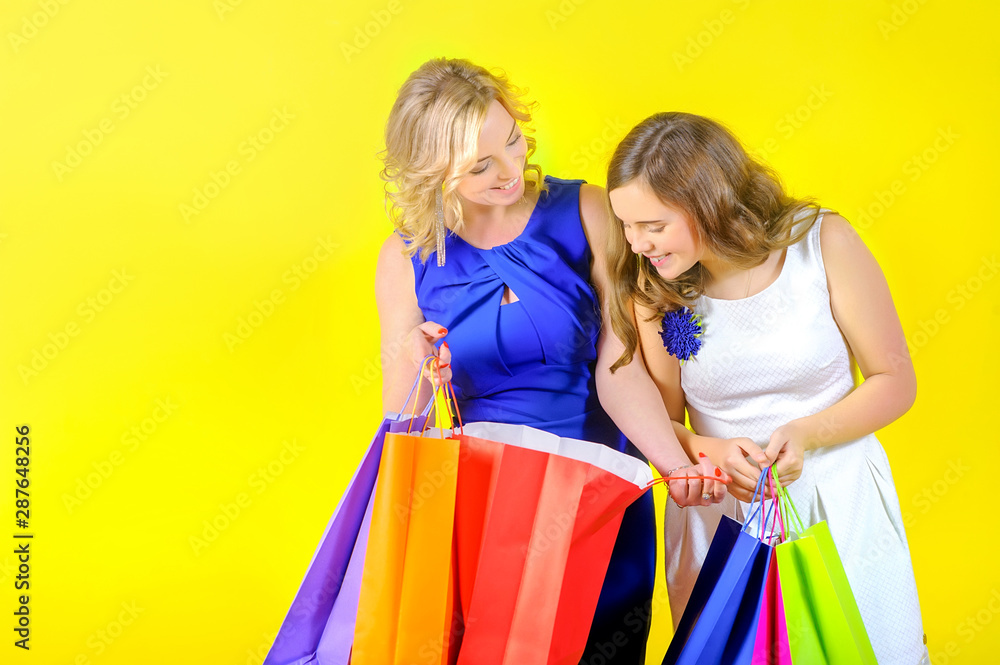 Cute blonde girl holds shopping bags in her hands, shows purchases to her daughter and smiles Cute blonde girl holds shopping bags in her hands, shows purchases to her daughter and smiles