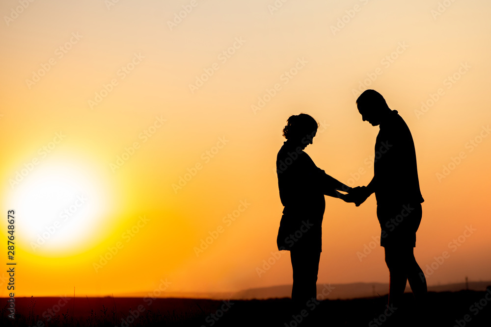 Silhouette of a man and a pregnant woman. A loving couple holding hands.