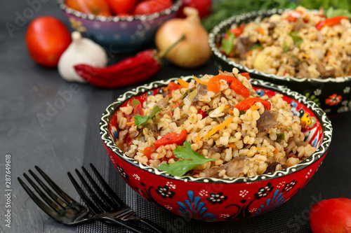 Bulgur with mushrooms and vegetables in a two bowls on a dark background, vegetarian oriental dish, horizontal orientation