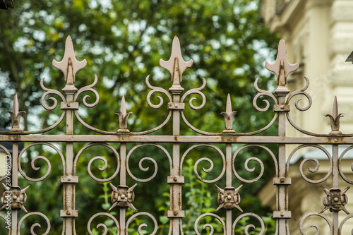 metal carved vintage fence with sharp spiers on a blurry background of architecture in the daytime