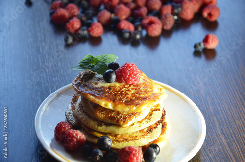 Pancakes with berries and maple syrup with raspberries and blueberries on a black background