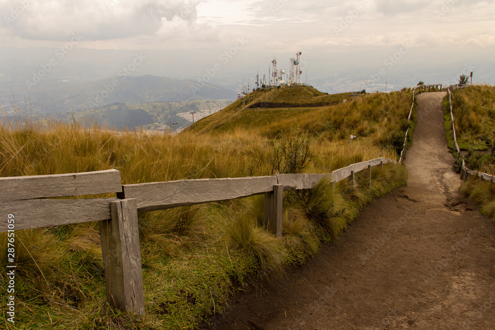 It is a road at the top of the mountain that arrives by cable car, in Quito, Ecuador. The road is bordered by wooden railings is a cloudy day.