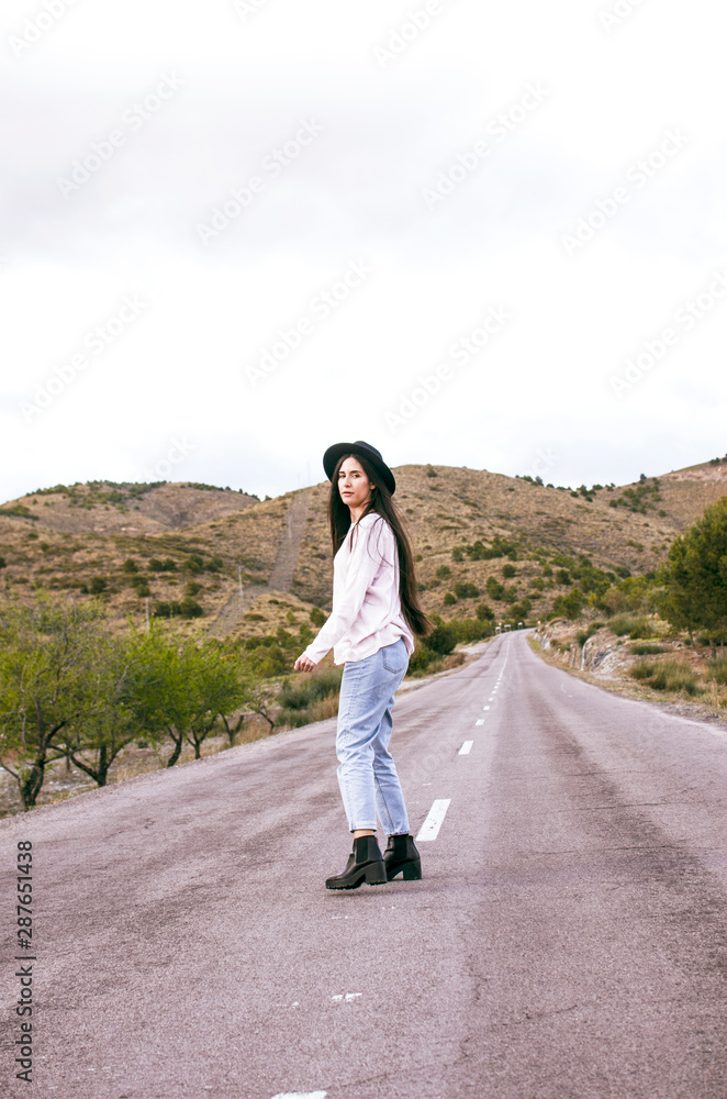 young woman with hat crossing an empty road in a rural area