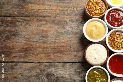 Set of different delicious sauces on wooden table, top view. Space for text