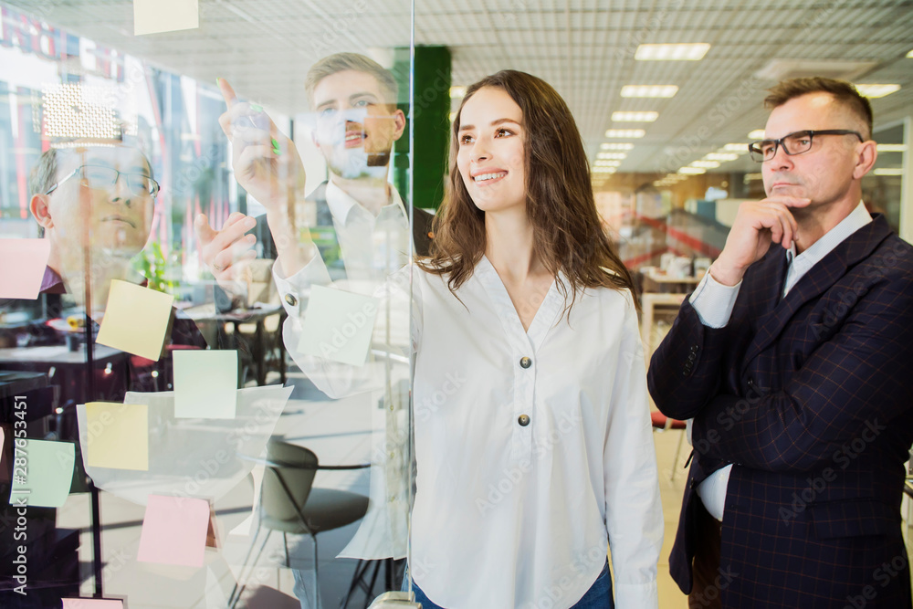 Obraz premium woman leader making notes on paper sticks from glass wall in office