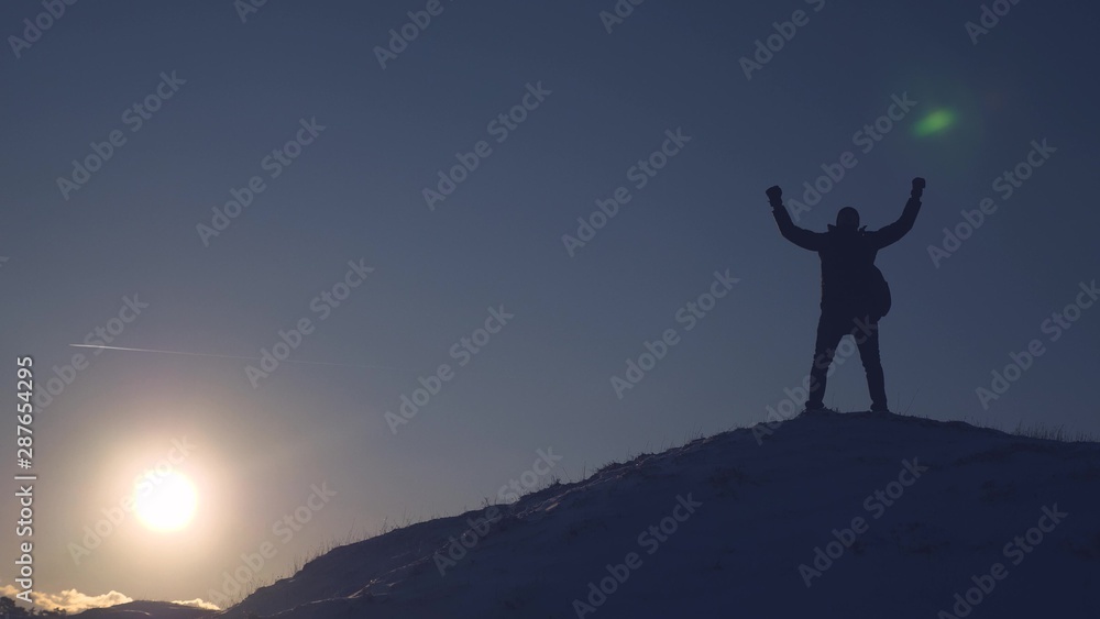 Mountaineer Journey to mountains in winter. Traveler climbs mountain peak. tourist stands on high snowy mountain, waves his hands and rejoices at victory at sunset. Alpenist travels hiking.
